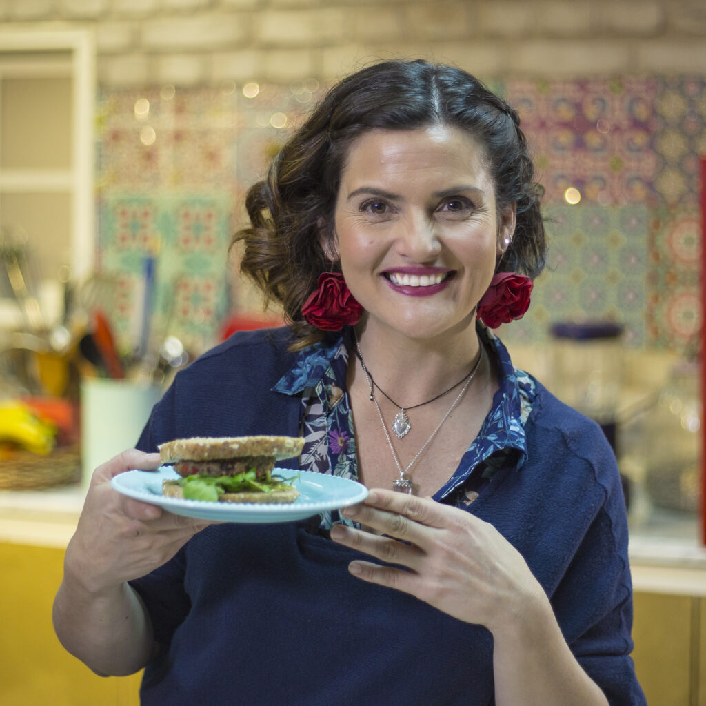Connie Achurra levanta un plato en sus manos para mostrar un sándwich.