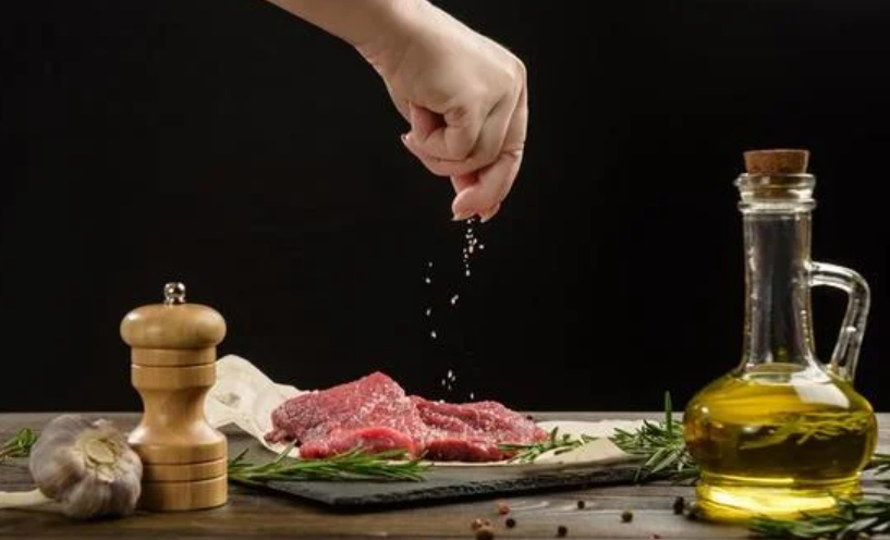 Mano de una mujer sazonando recortes de carne cruda